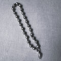 Sterling silver bead mala for a small idol with an engraved leaf drop, large size, on a grey surface.