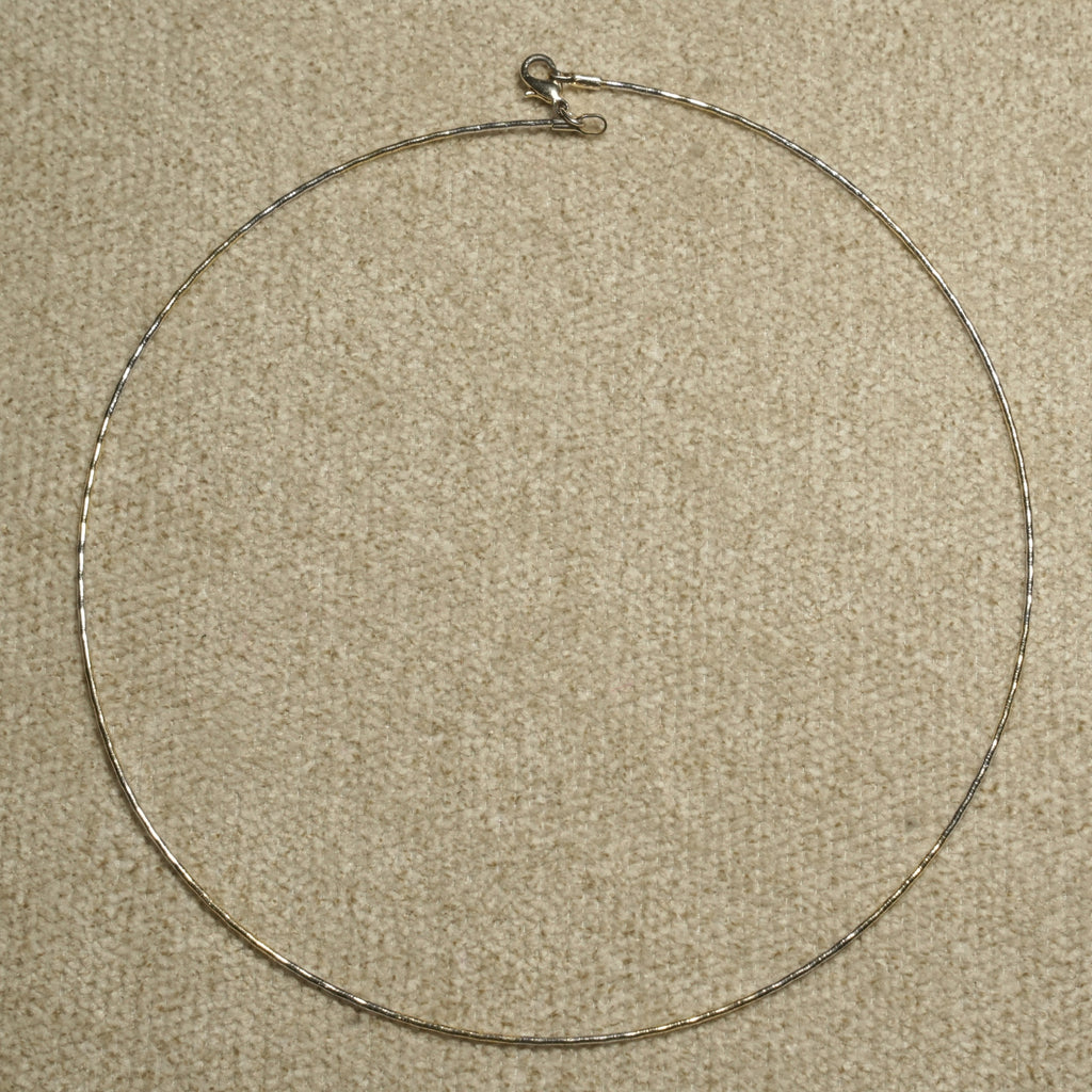 Full circle view of the fine sterling silver wire collar laid flat on beige fabric, showing its lobster clasp at the top.