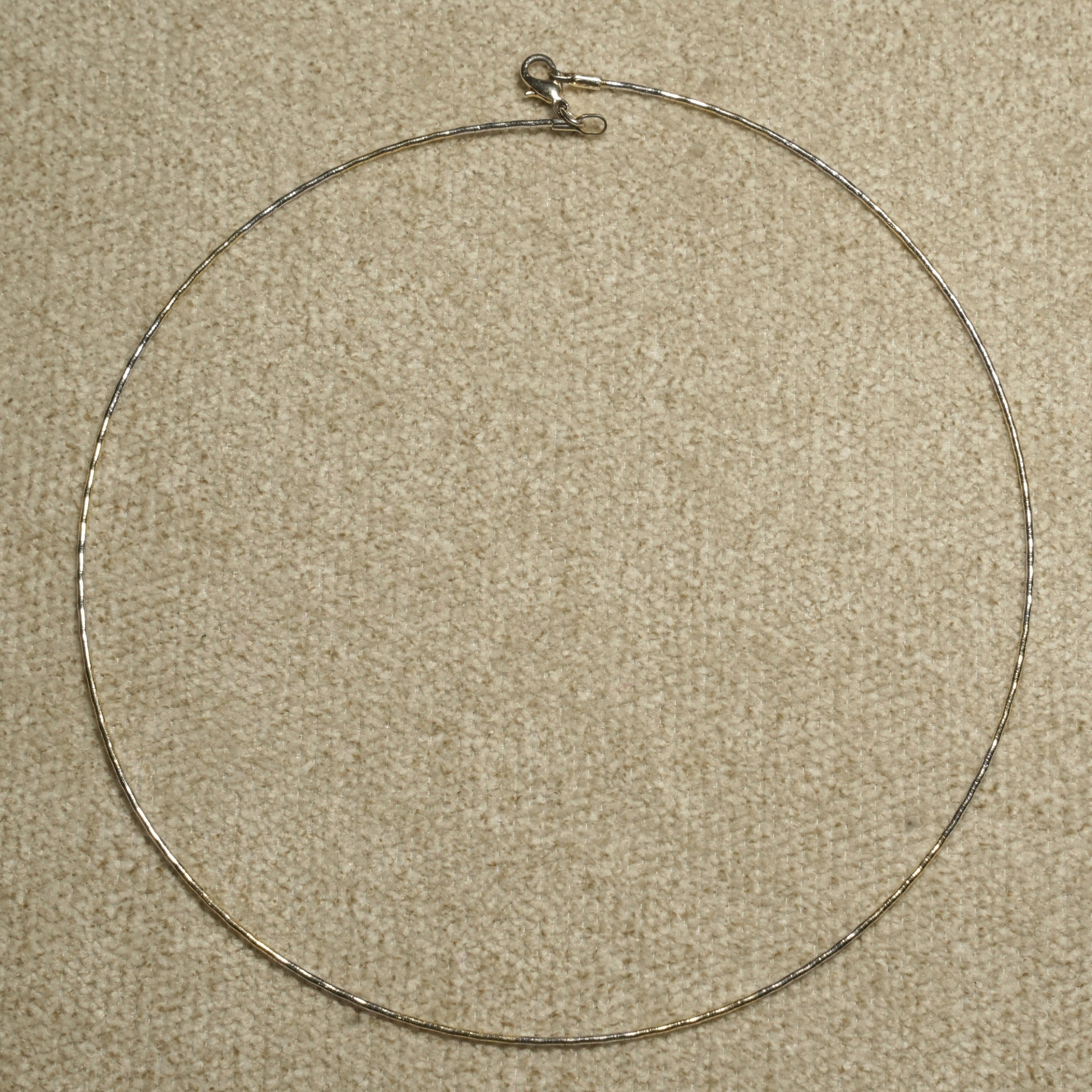 Full circle view of the fine sterling silver wire collar laid flat on beige fabric, showing its lobster clasp at the top.