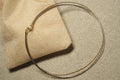 Tri-tone sterling silver wire collar necklace in gold-tone, rose gold-tone and oxidised grey, coiled over a woven jute pouch.