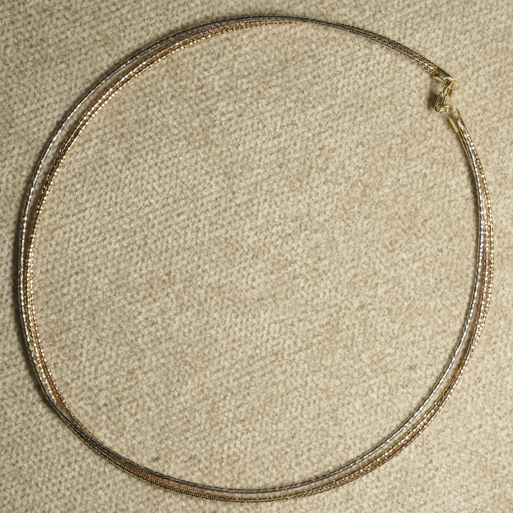Full circle view of the three-wire collar laid flat on beige fabric, its mixed tones meeting at a gold-tone clasp.