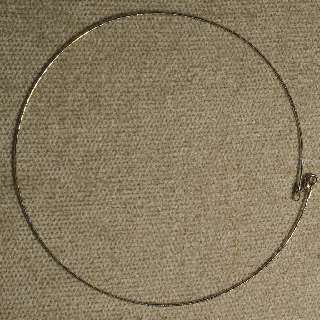 Full circle view of the slim sterling silver wire collar laid flat on beige fabric, showing the small lobster clasp.