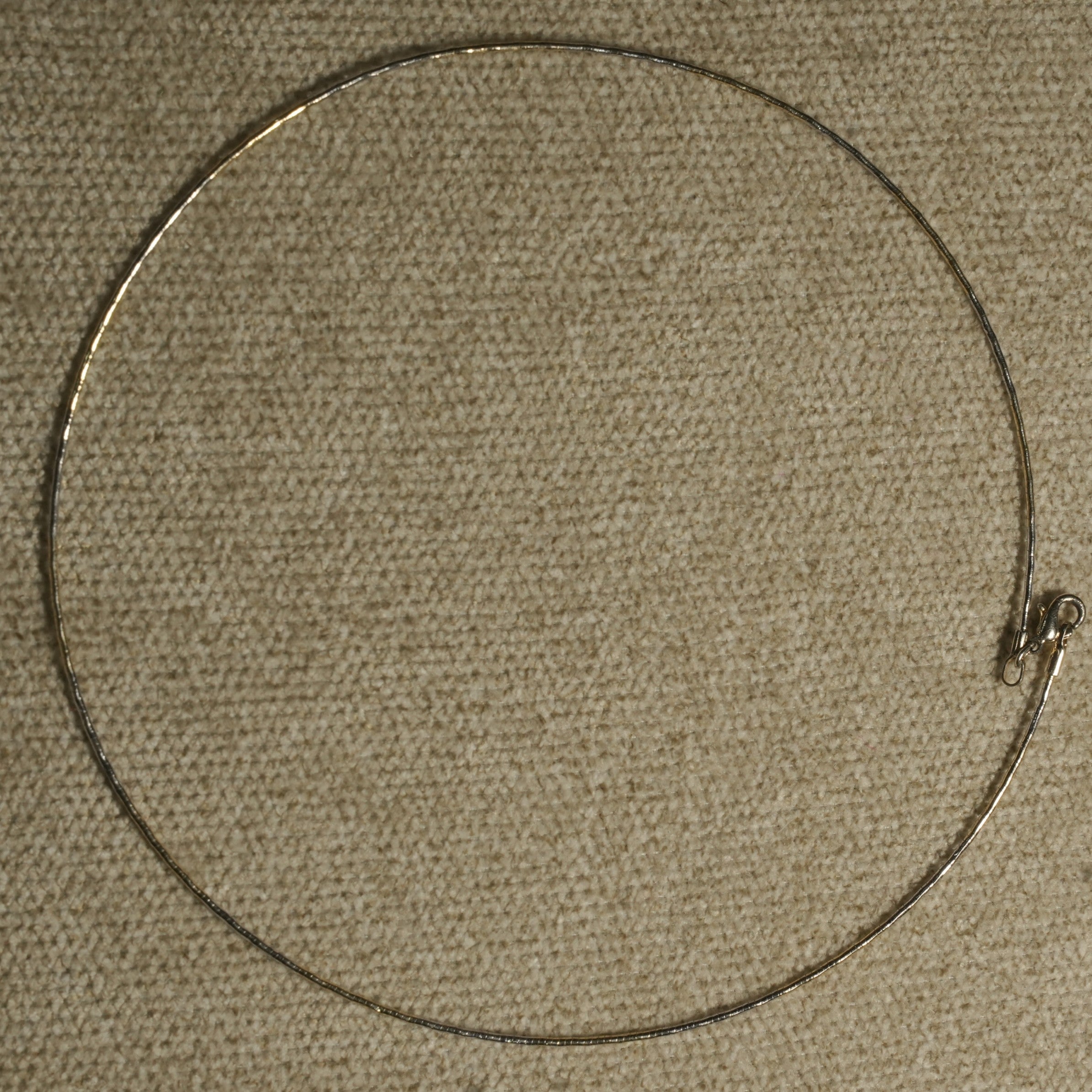 Full circle view of the slim sterling silver wire collar laid flat on beige fabric, showing the small lobster clasp.