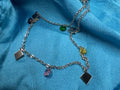 Sterling silver station necklace on blue satin, with faceted pink, yellow and green stones hanging between flat kite-shaped plaques.