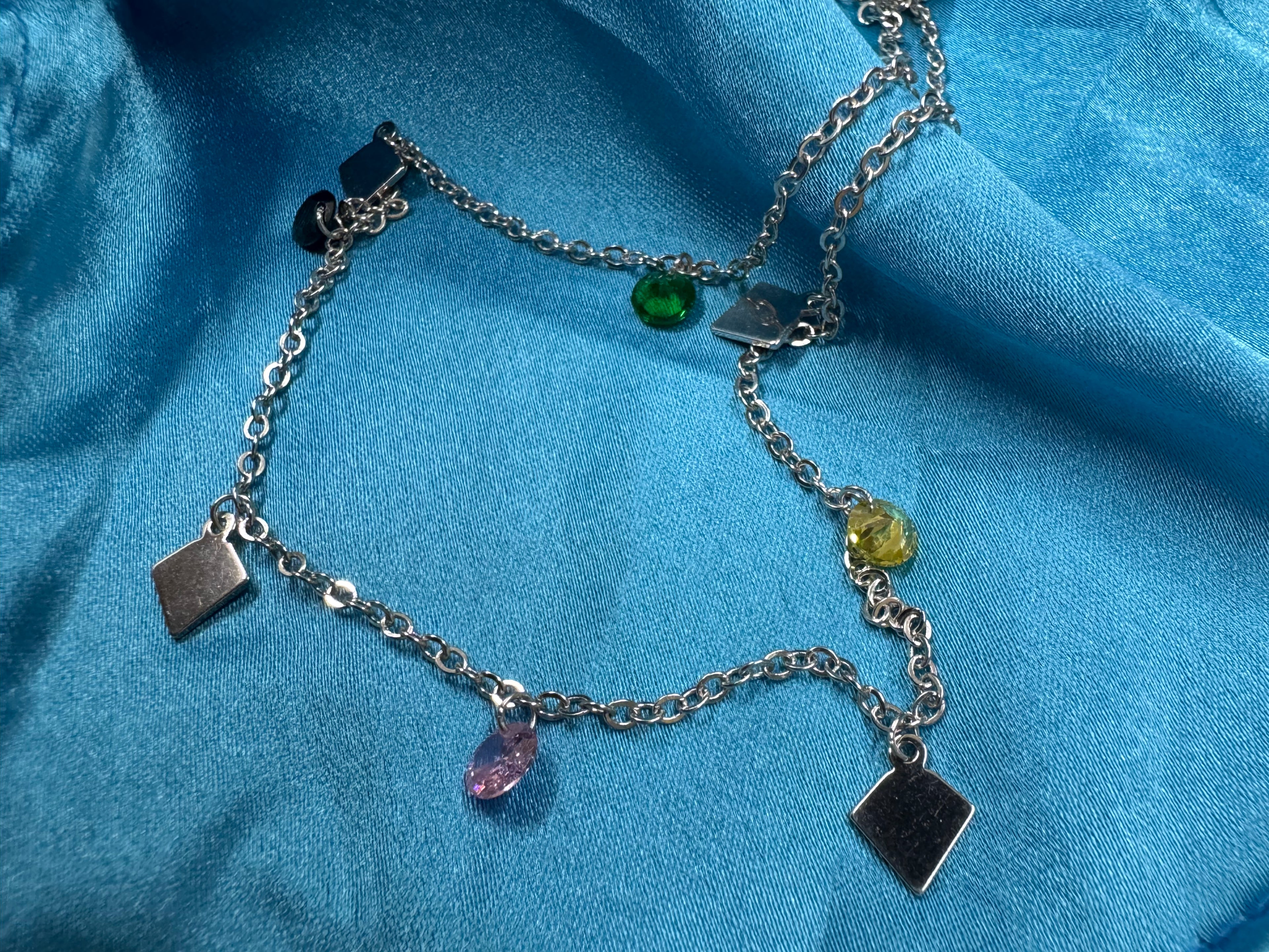 Sterling silver station necklace on blue satin, with faceted pink, yellow and green stones hanging between flat kite-shaped plaques.