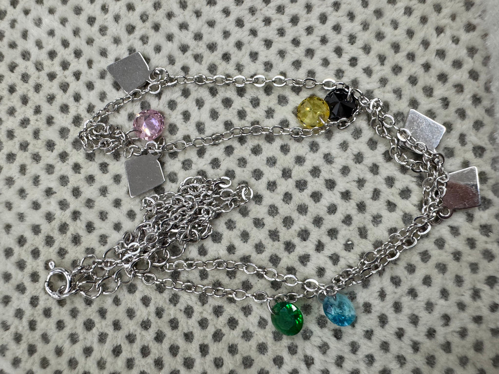 The full sterling silver cable chain necklace coiled on spotted cream fabric, with its spring ring clasp at the lower left.