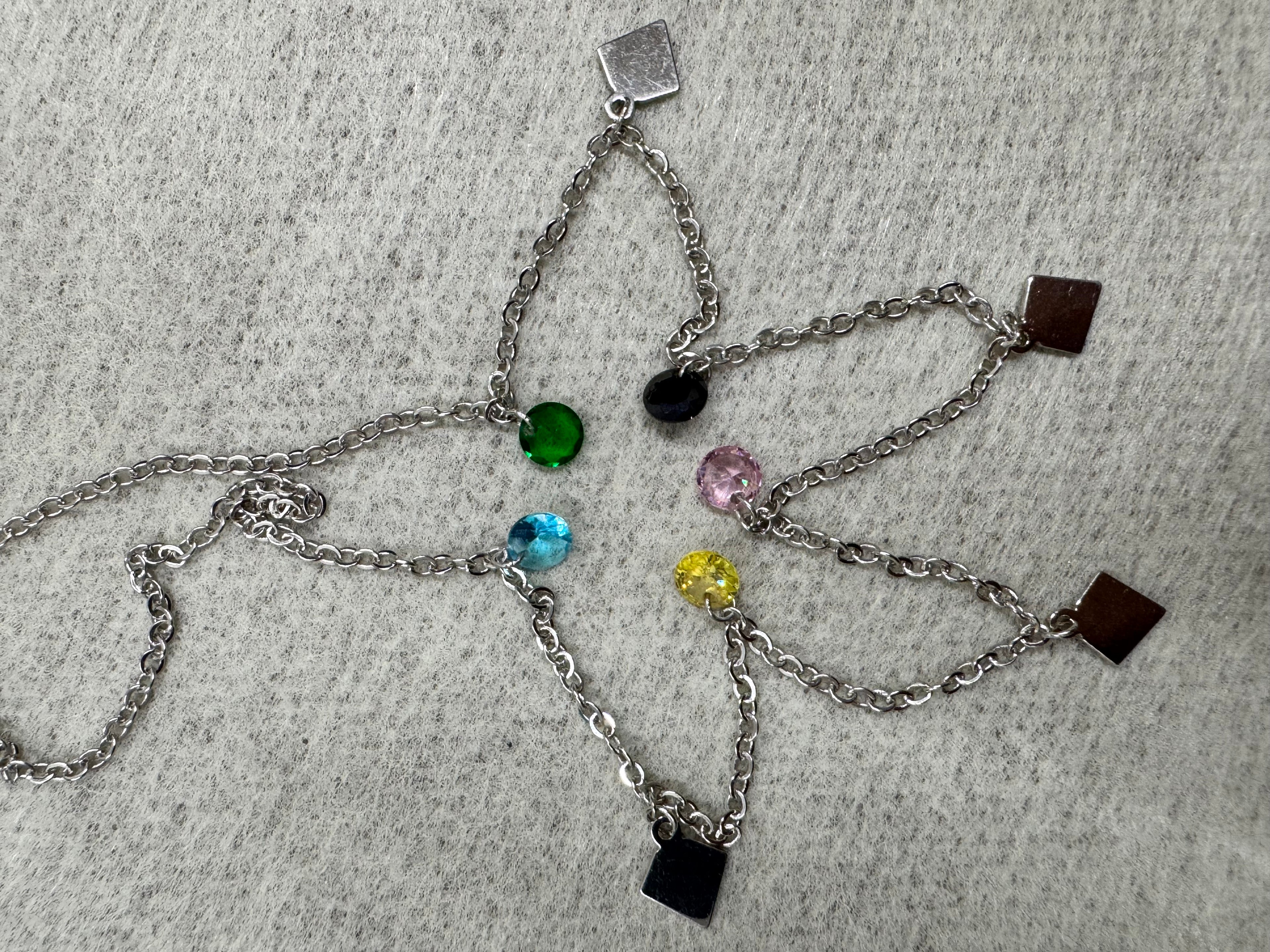Sterling silver necklace spread open on grey felt, showing the spacing of the coloured stones and the polished kite plaques.
