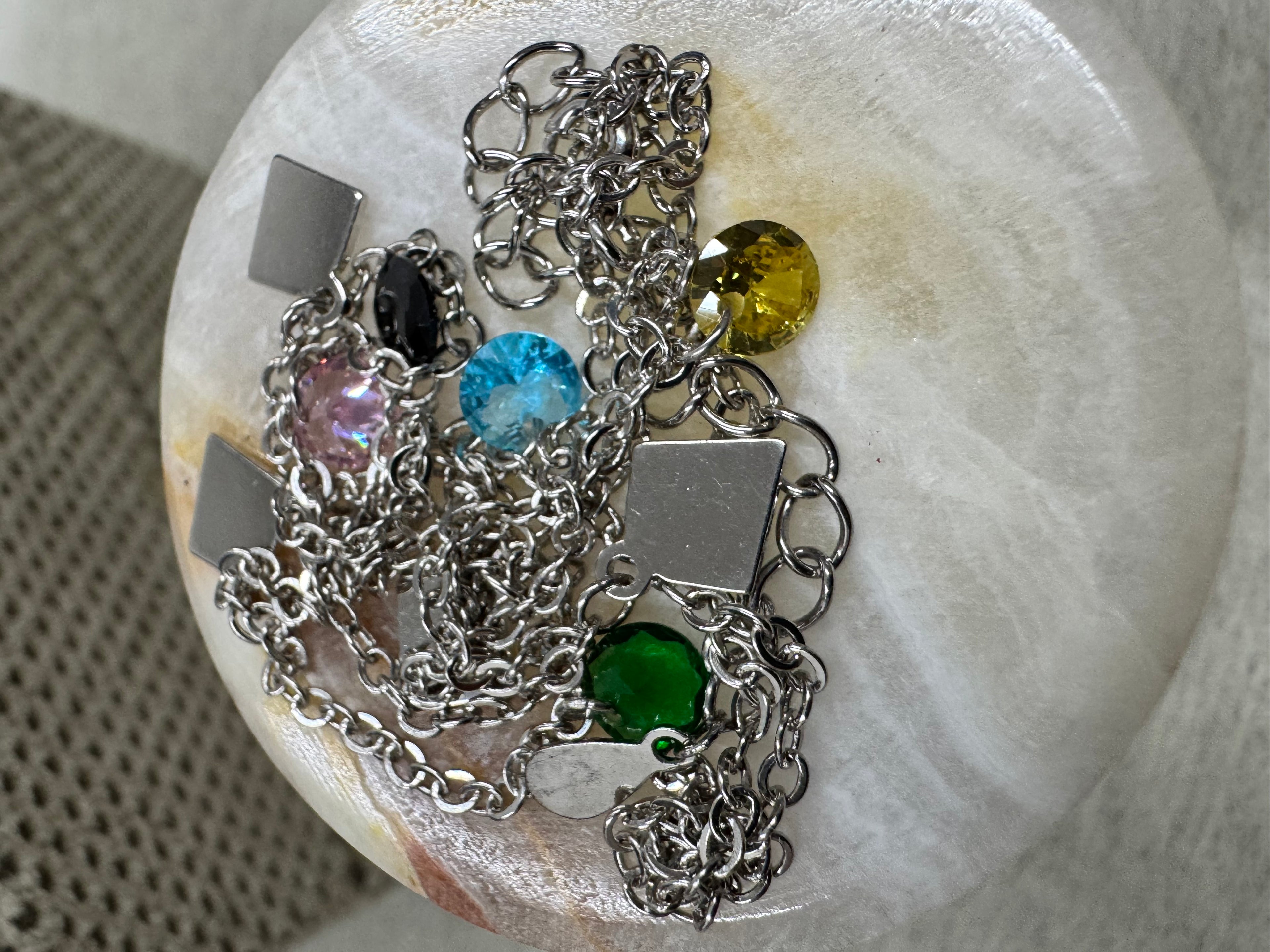 Close view of a yellow faceted stone and a kite-shaped silver plaque on the necklace, gathered on a marble dish.