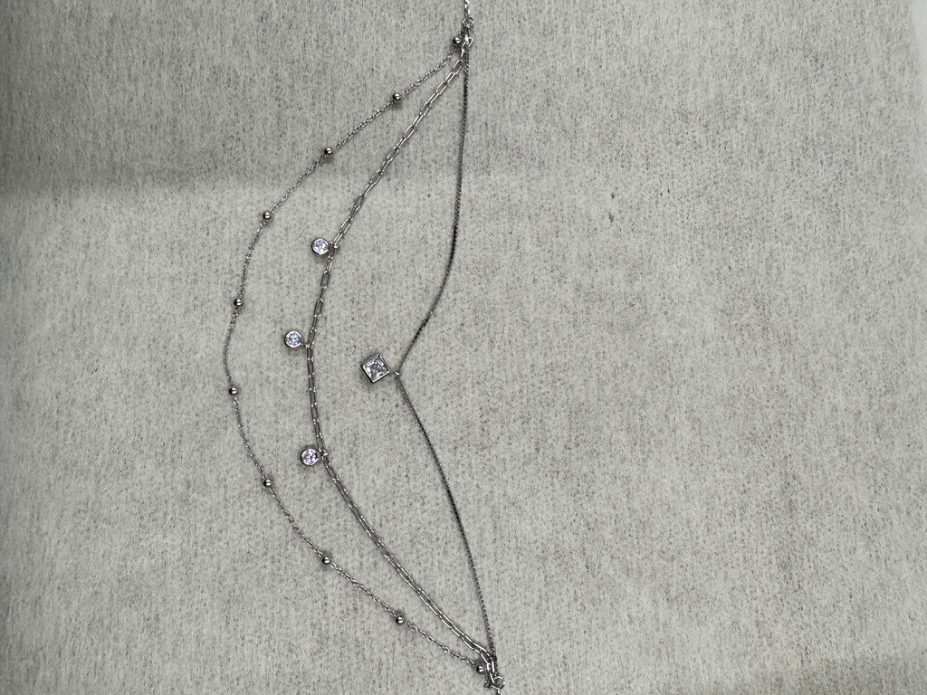 The sterling silver layered necklace hung vertically on grey fabric, the three strands falling from one clasp at different lengths past the square and round cubic zirconia stones.
