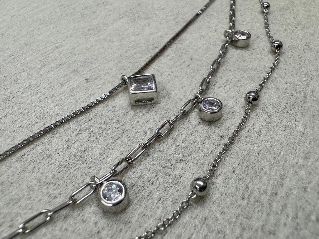 Close view of the bezel-set square cubic zirconia on the sterling silver box chain, with two round bezel-set stones and the satellite bead chain behind.