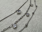 Close view of the bezel-set square cubic zirconia on the sterling silver box chain, with two round bezel-set stones and the satellite bead chain behind.