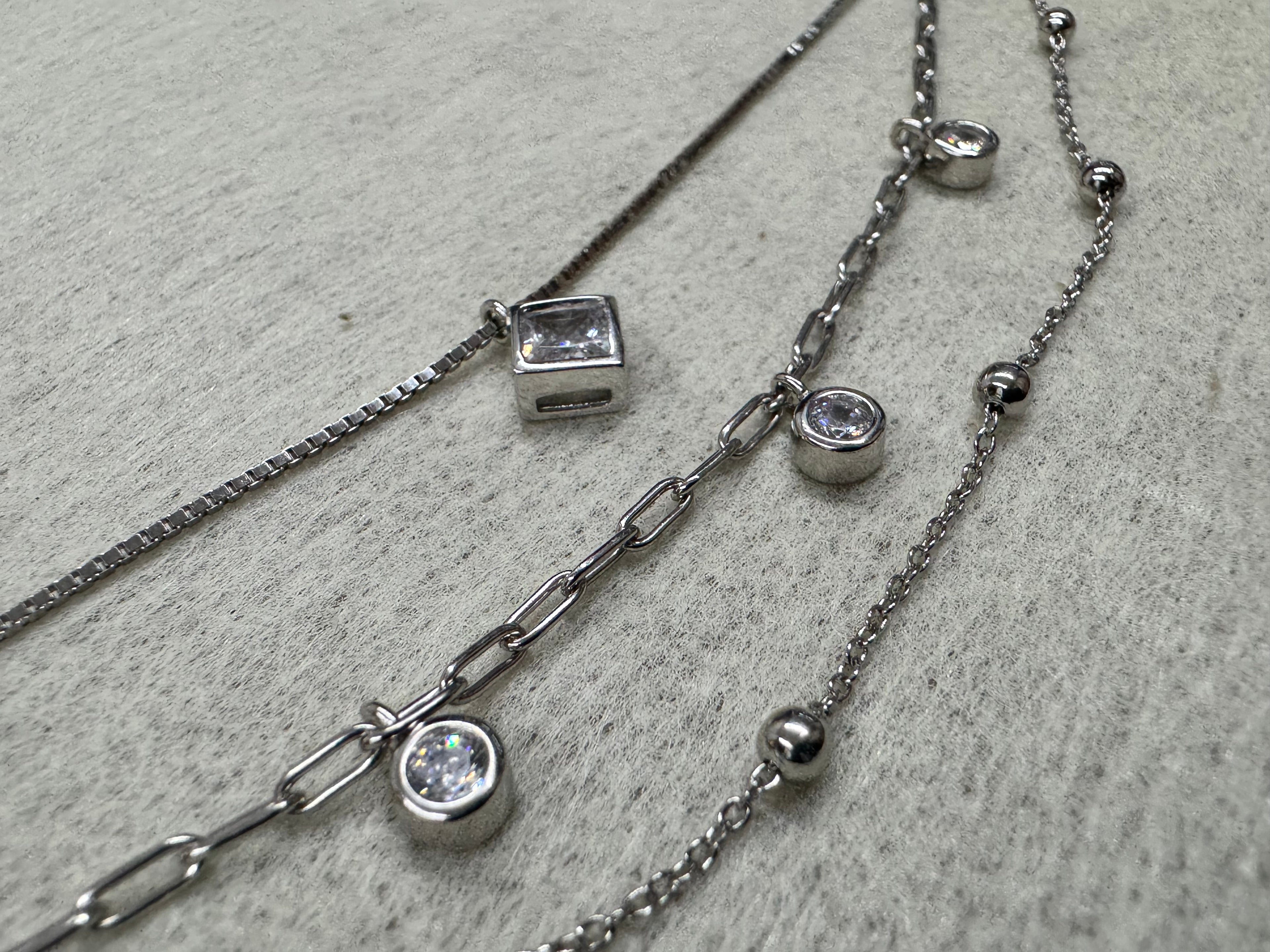 Close view of the bezel-set square cubic zirconia on the sterling silver box chain, with two round bezel-set stones and the satellite bead chain behind.