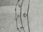Detail of the three strands of the sterling silver necklace running side by side on grey fabric, with the square cubic zirconia on the box chain and two round stones on the paperclip chain.