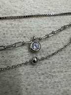 Close view of the three chain constructions of the sterling silver necklace on grey fabric: box chain, paperclip chain with a round cubic zirconia and satellite chain with a polished silver ball.