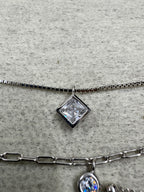 Macro of the square bezel-set cubic zirconia sitting on the fine box chain of the sterling silver necklace, the paperclip strand and a round stone at the right edge.