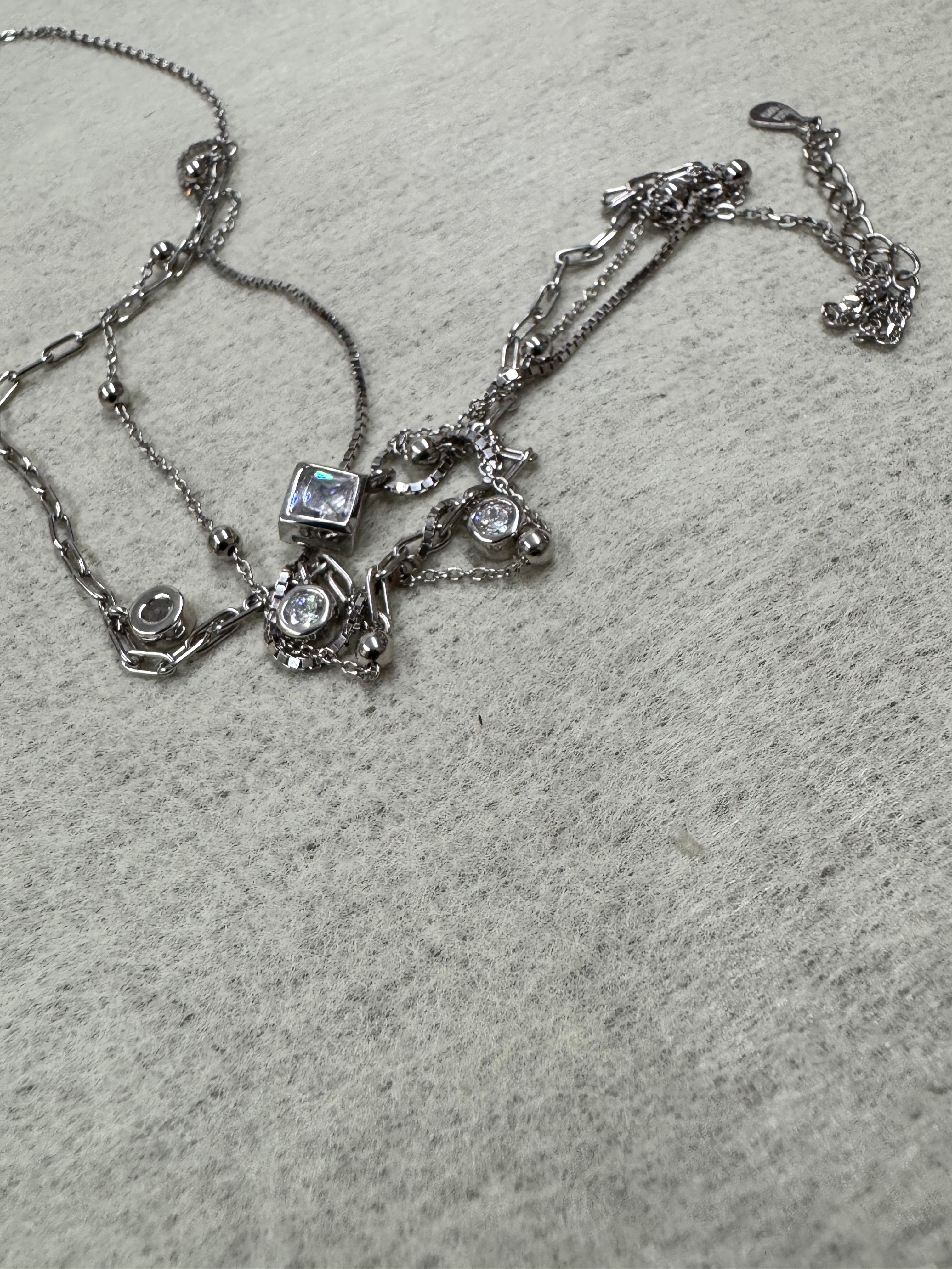 The full three-strand sterling silver necklace loosely coiled on grey fabric, showing the clasp, extender chain and all stone stations.