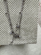 The sterling silver layered necklace lying diagonally across cream fabric with grey dots, the square cubic zirconia and two round drops gathered near the centre.
