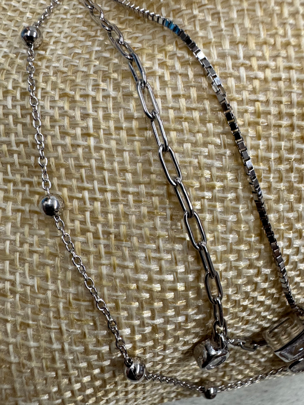 Detail of the box, paperclip and satellite chains of the sterling silver necklace on cream woven fabric, with the polished silver balls and one bezel-set cubic zirconia visible.