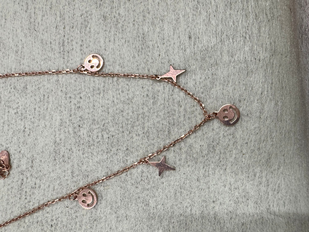 Rose-tone sterling silver necklace on grey felt, pierced smiley discs and flat stars spaced along a fine cable chain.