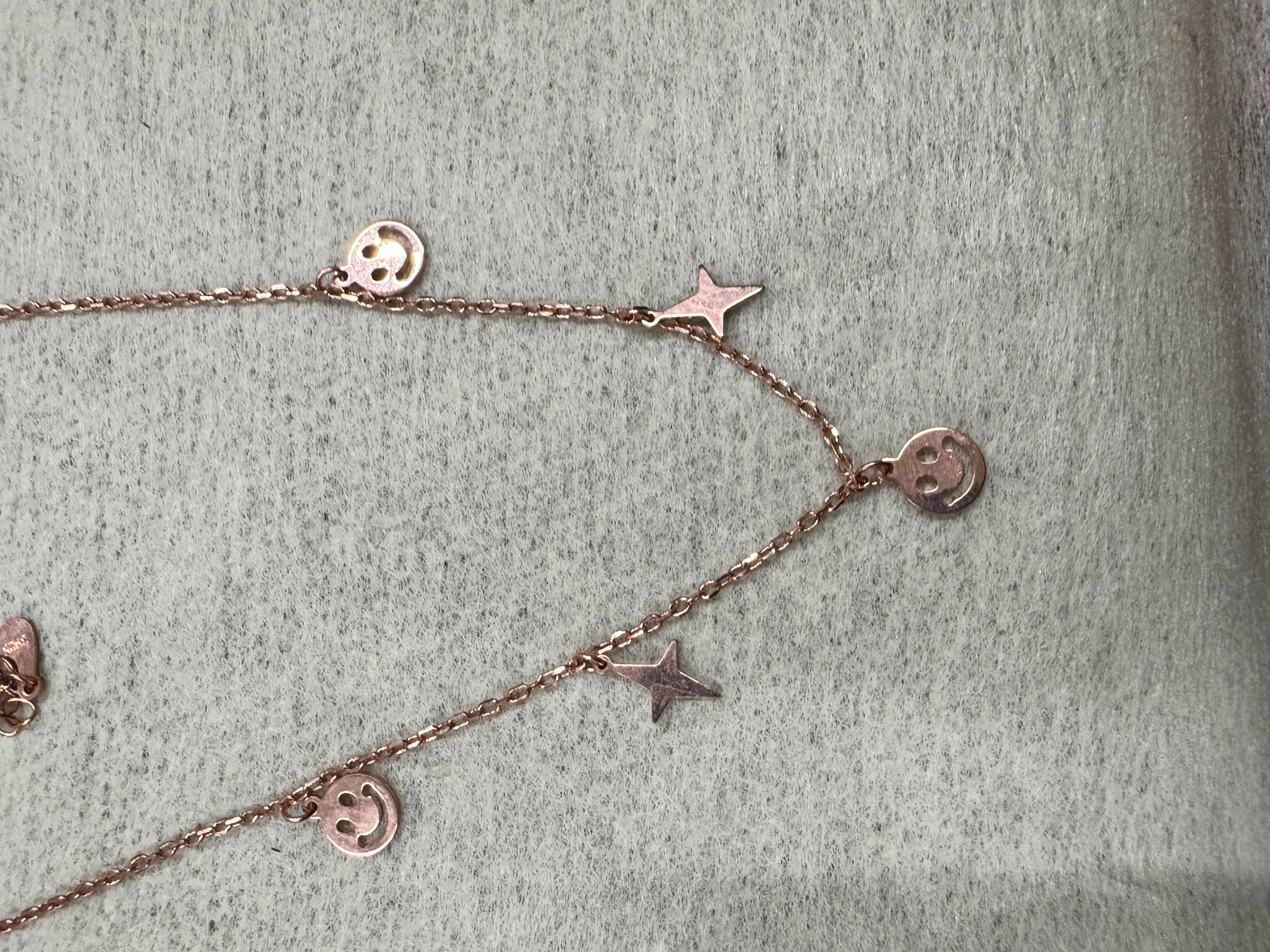 Rose-tone sterling silver necklace on grey felt, pierced smiley discs and flat stars spaced along a fine cable chain.