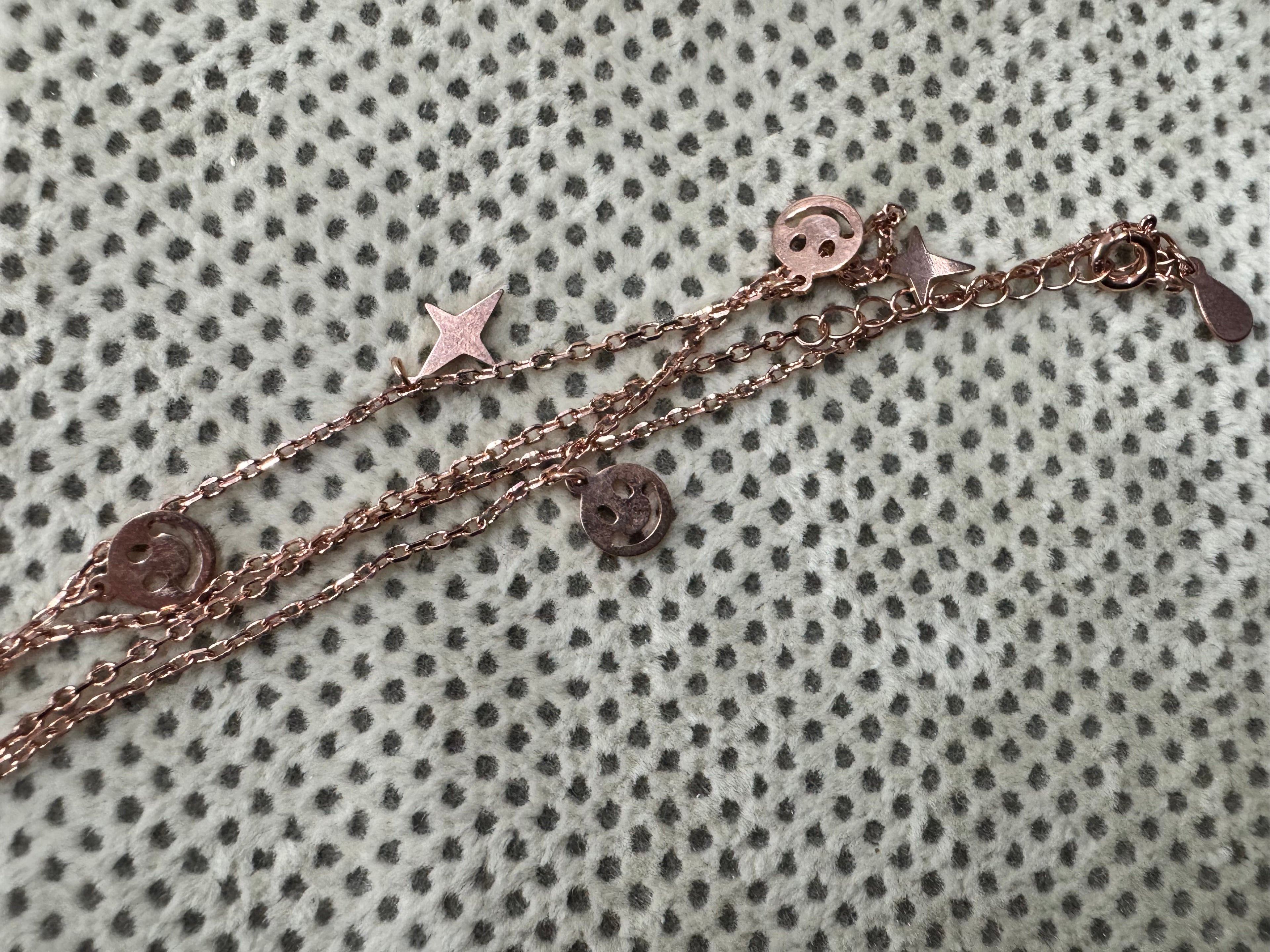 The rose-tone sterling silver station necklace laid on spotted cream fabric, with the clasp, extender chain and hanging tag at the right.
