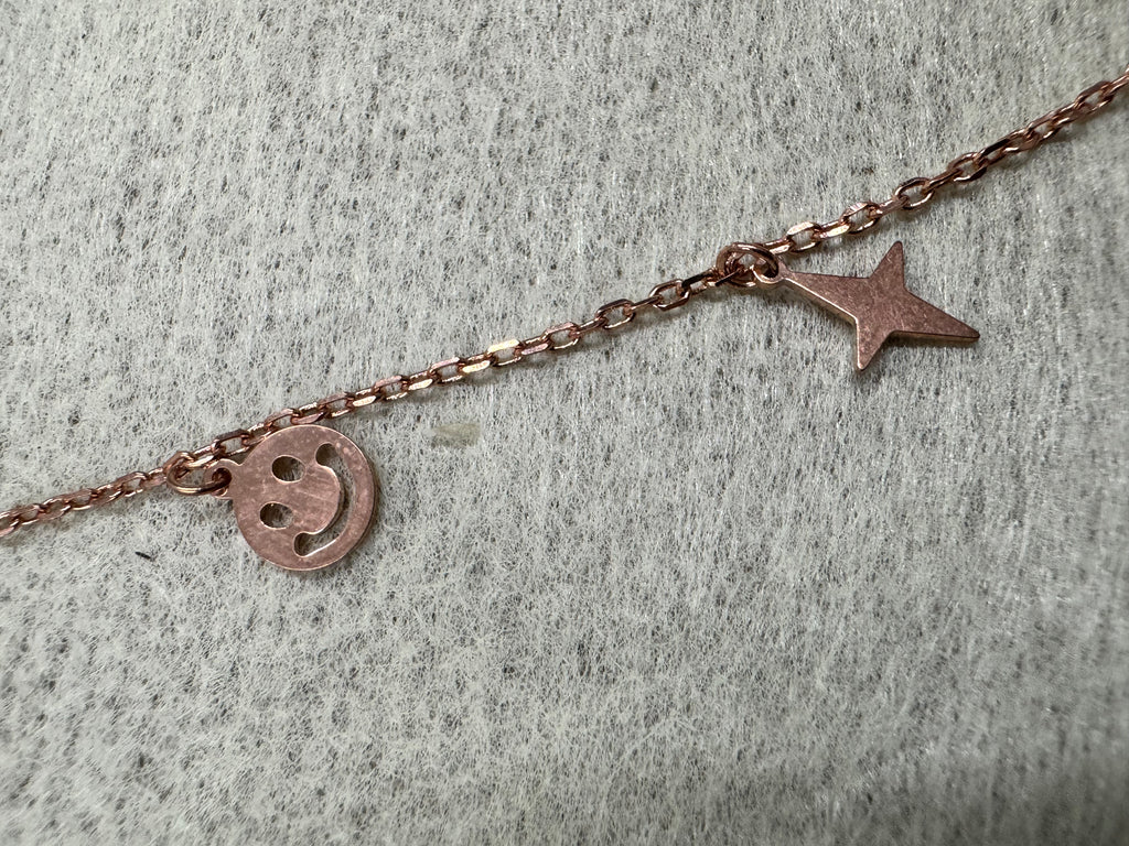 Close view of a pierced smiley disc and a four-pointed star on the rose-tone sterling silver chain.