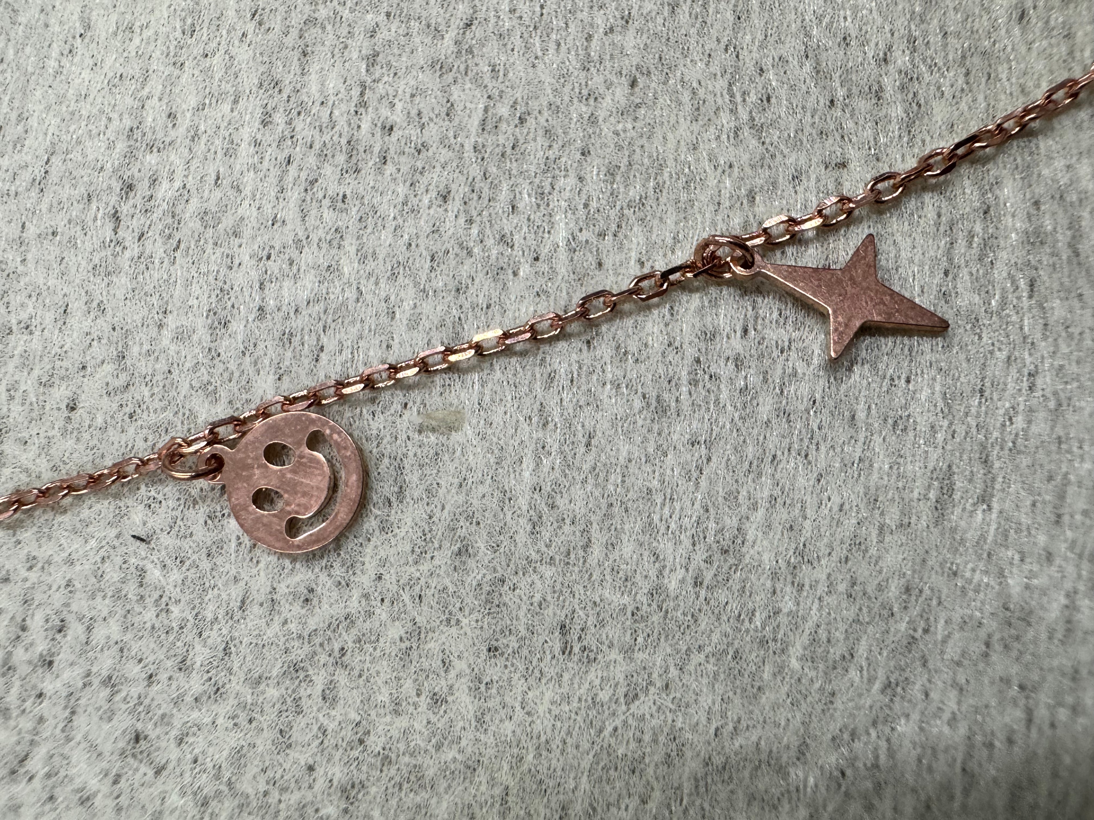 Close view of a pierced smiley disc and a four-pointed star on the rose-tone sterling silver chain.