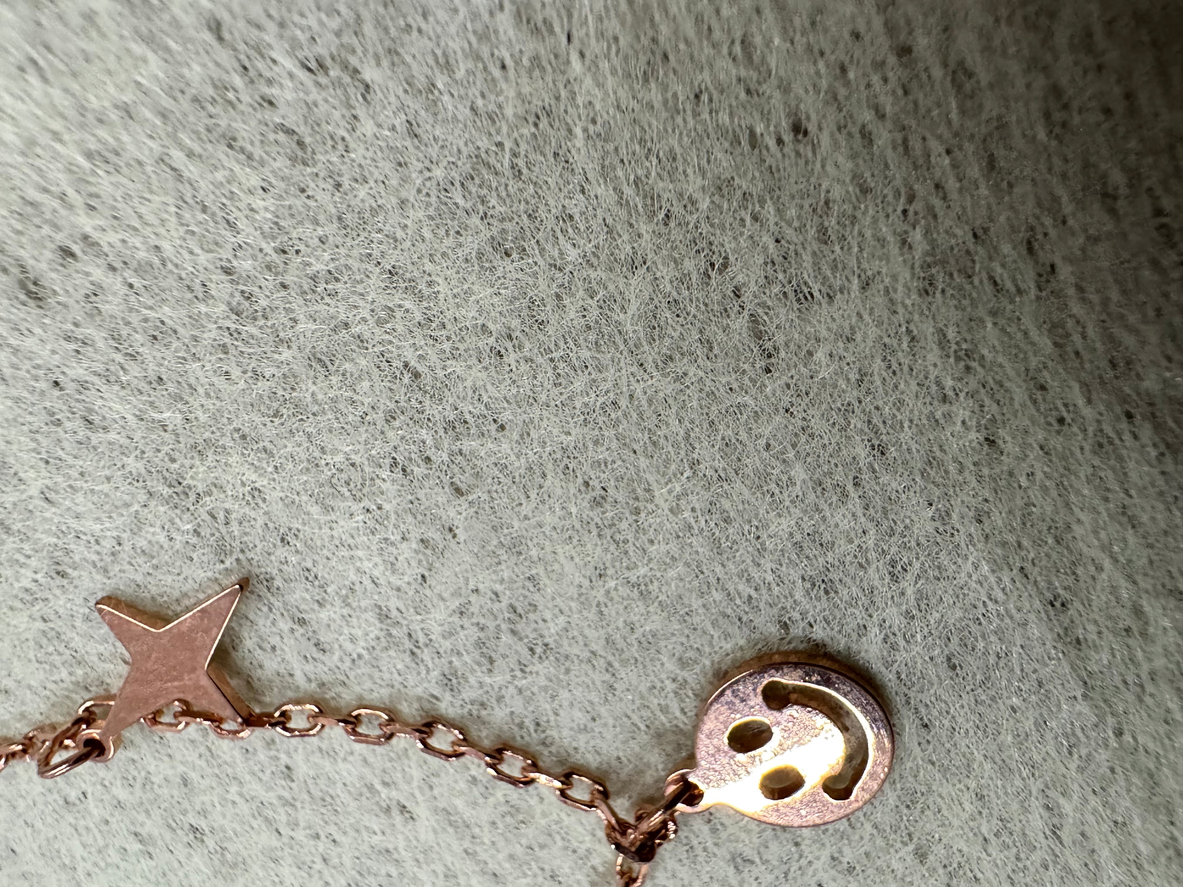 A four-pointed star and a smiley disc hanging from the rose-tone sterling silver necklace against grey felt.