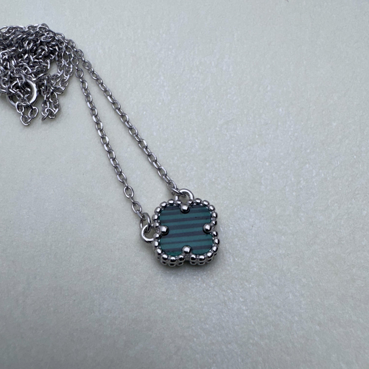 Sterling silver necklace with a green glass clover in a beaded frame, on a cable chain.