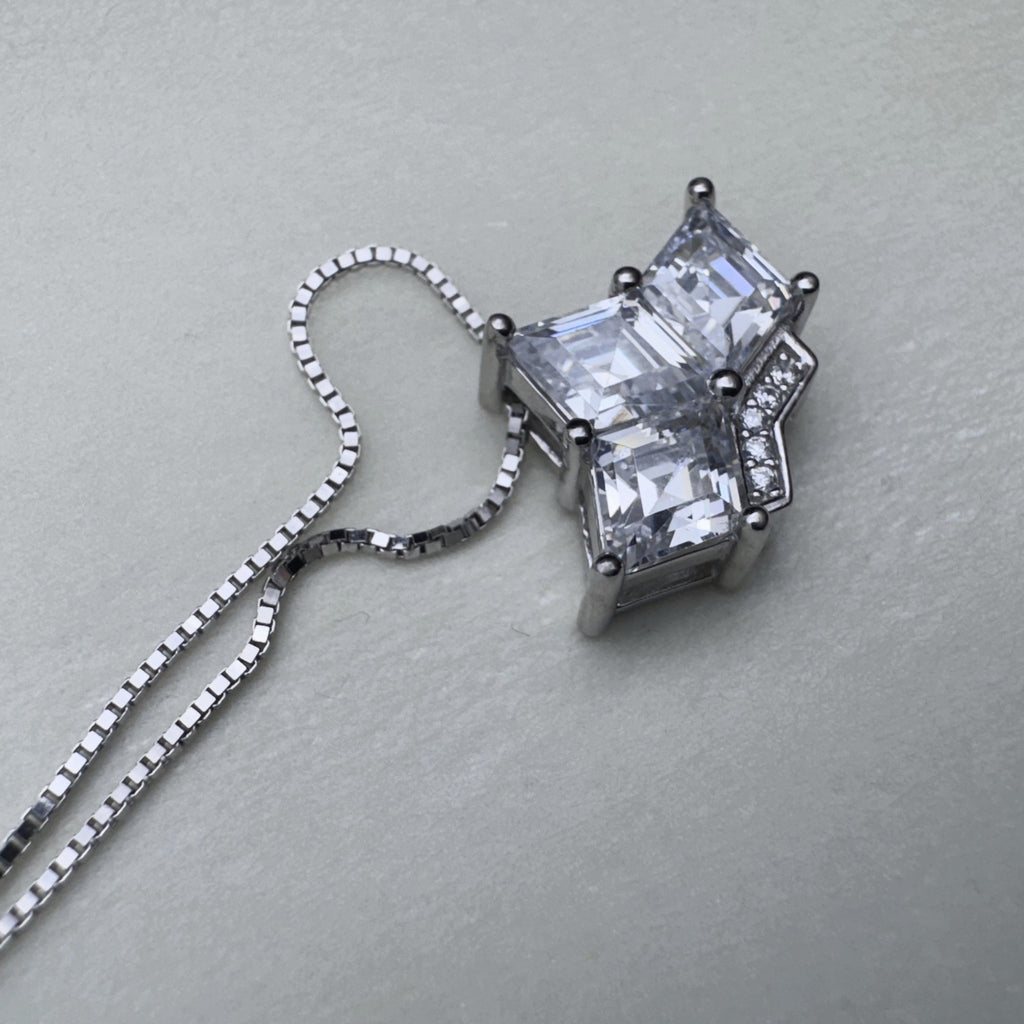 Close view of the three prong set princess-cut stones and the pave set band of the crown pendant.