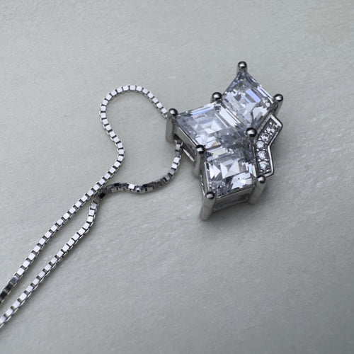 Close view of the three prong set princess-cut stones and the pave set band of the crown pendant.