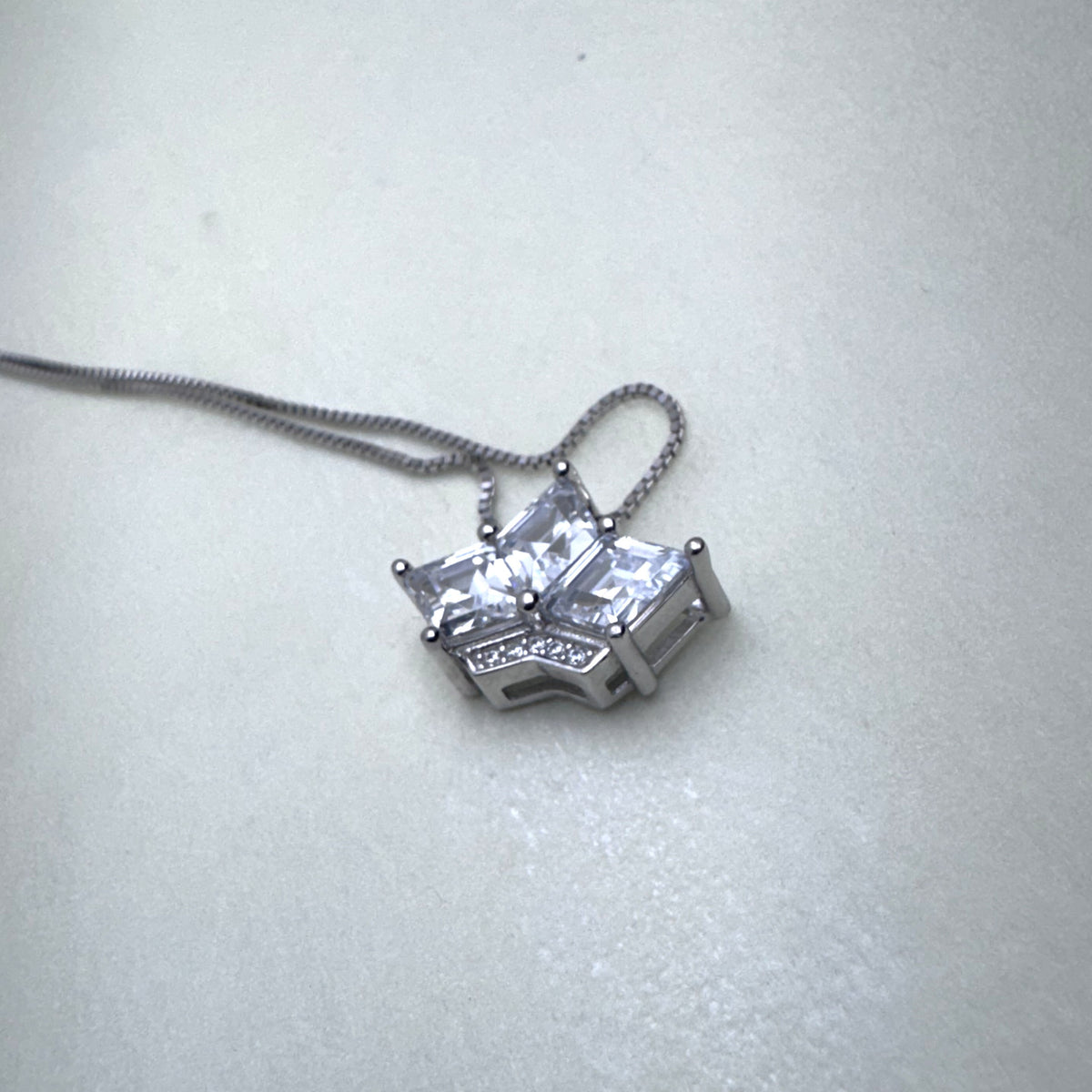 The crown pendant necklace laid on a pale surface with the chain looped above it.