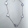 Sterling silver station necklace with five grey mother of pearl clovers laid out on a pale surface.