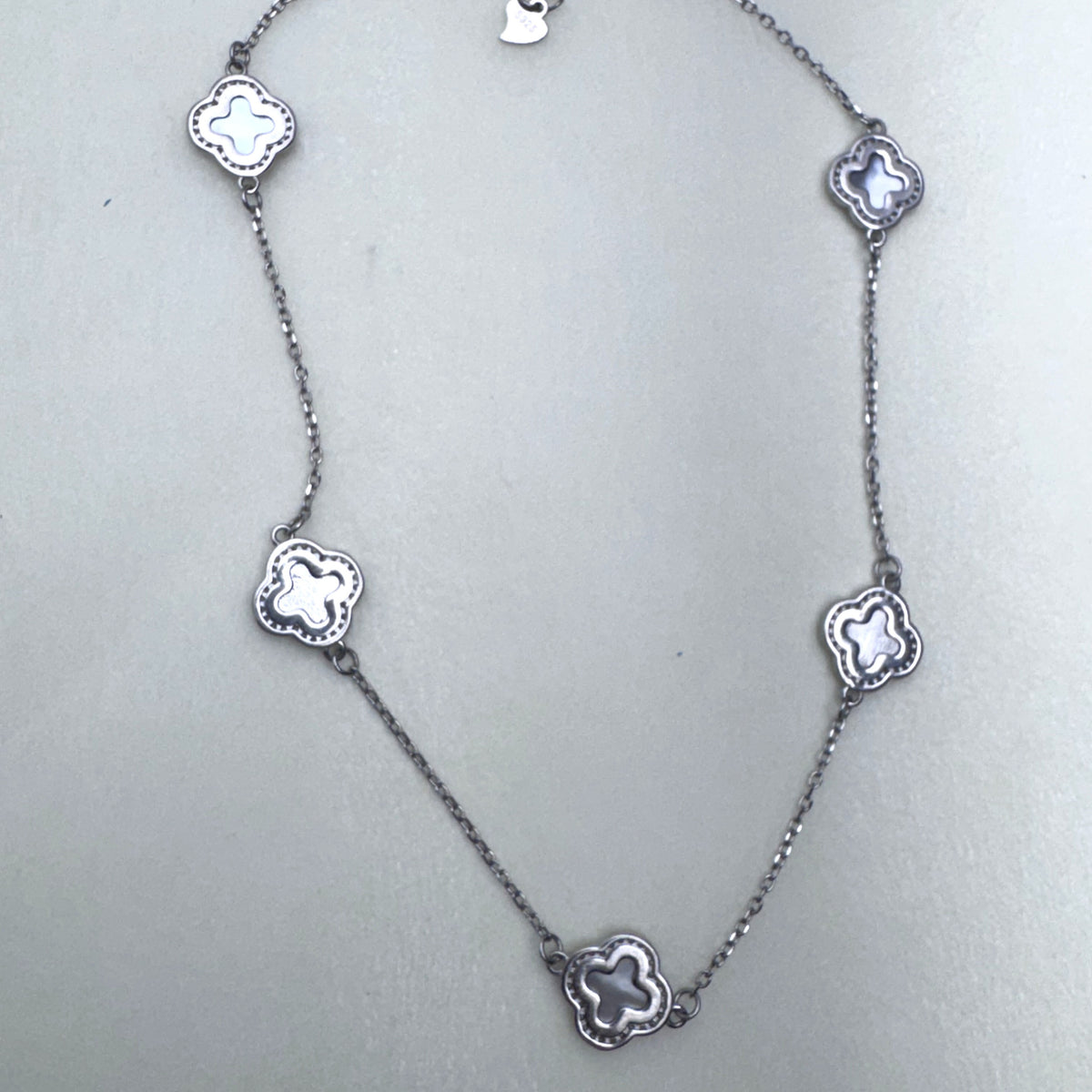 Sterling silver station necklace with five grey mother of pearl clovers laid out on a pale surface.