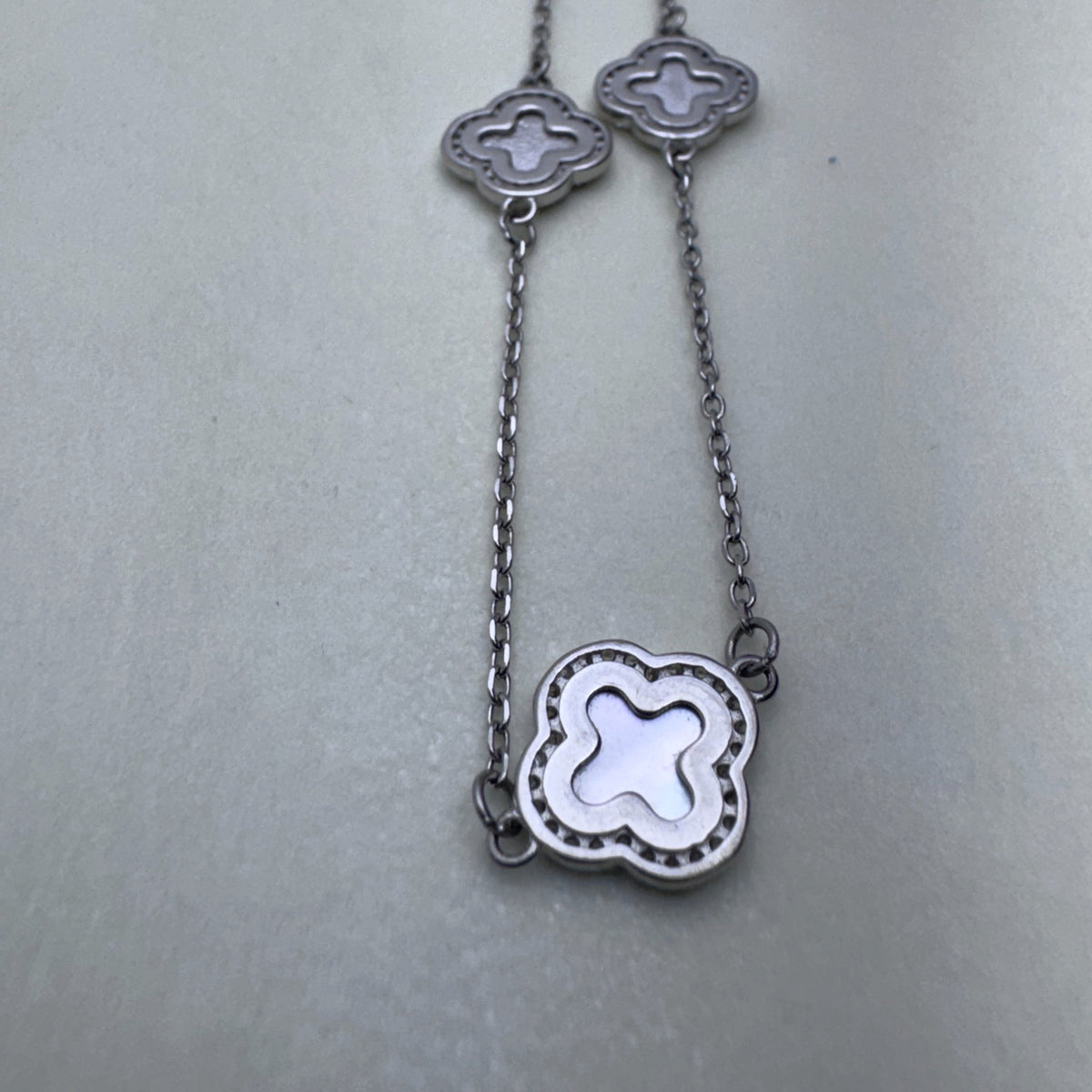 Close view of two mother of pearl clovers in beaded silver frames on the cable chain.