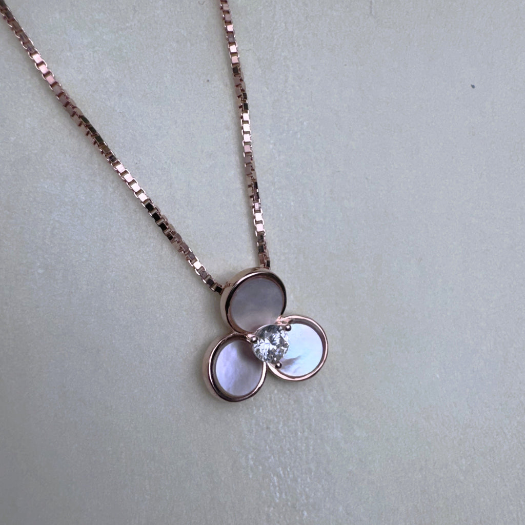 The three-petal mother of pearl pendant hanging from the rose-tone box chain.