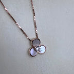 The three-petal mother of pearl pendant hanging from the rose-tone box chain.
