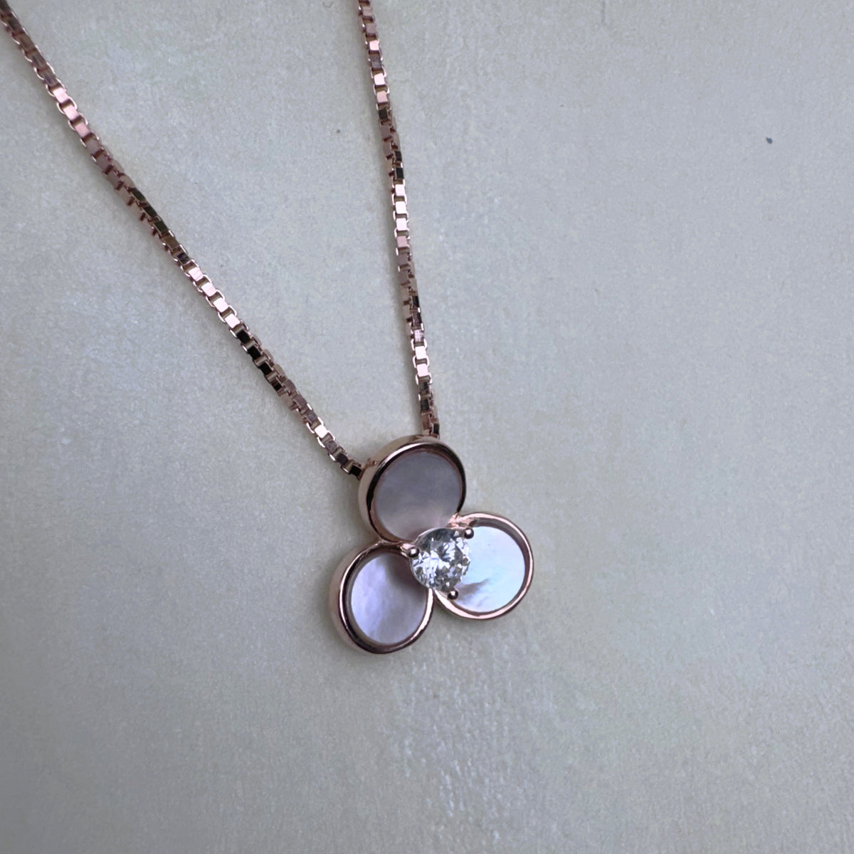 The three-petal mother of pearl pendant hanging from the rose-tone box chain.