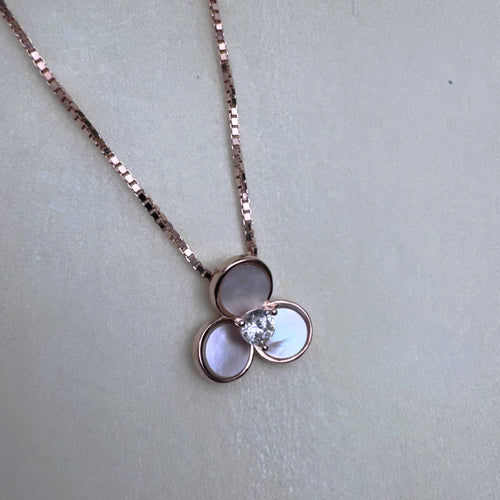 The three-petal mother of pearl pendant hanging from the rose-tone box chain.