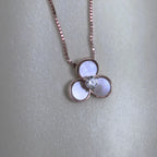 The rose-tone flower pendant seen from above on a pale surface.