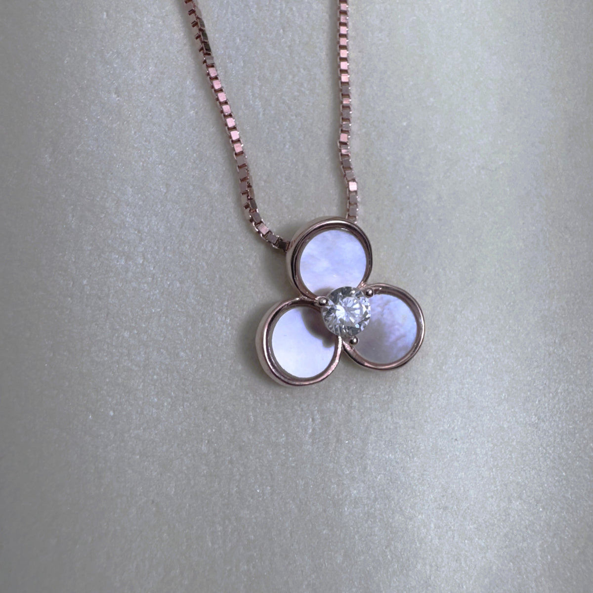 The rose-tone flower pendant seen from above on a pale surface.