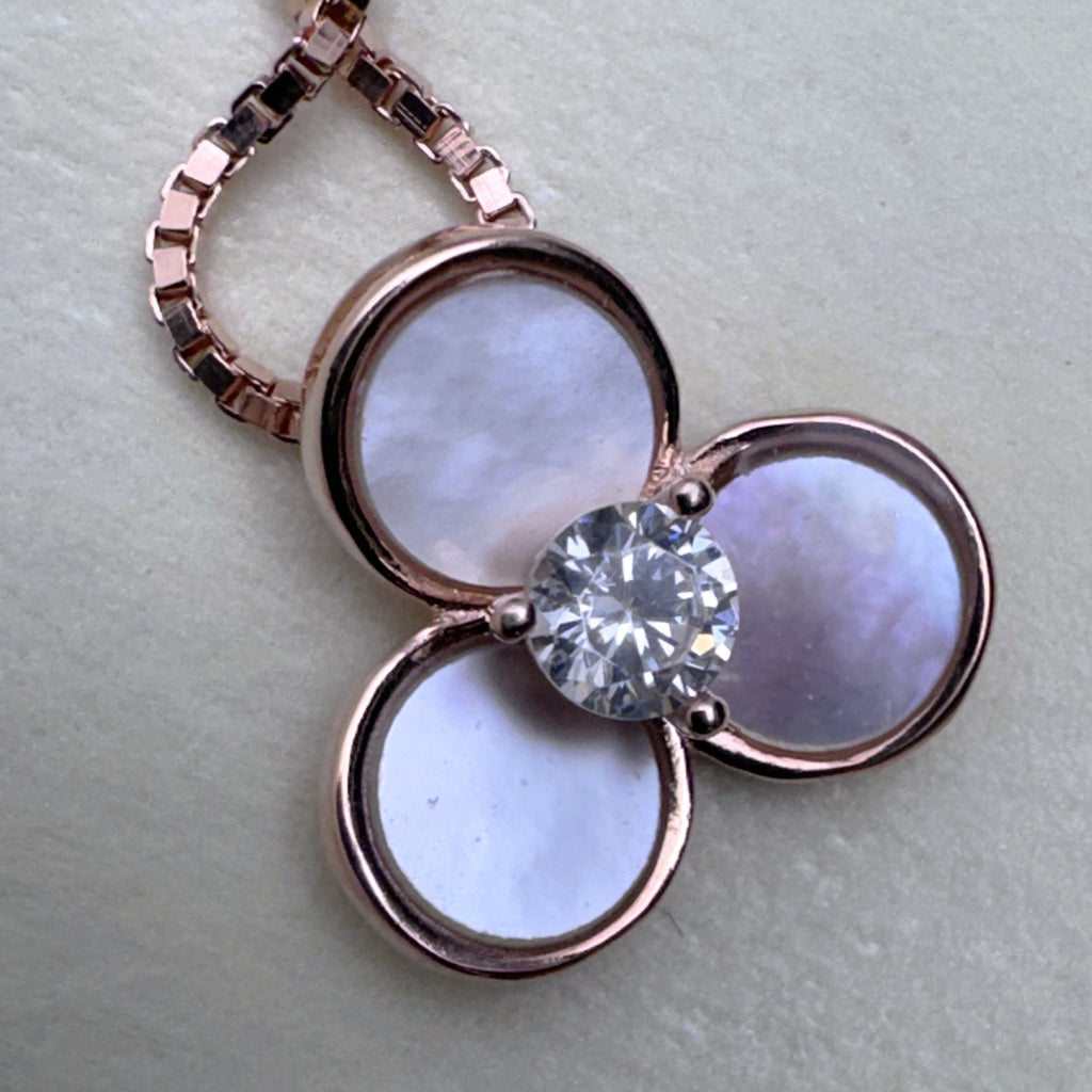 Close view of the pale mother of pearl petals in rose-tone bezels around the centre stone.