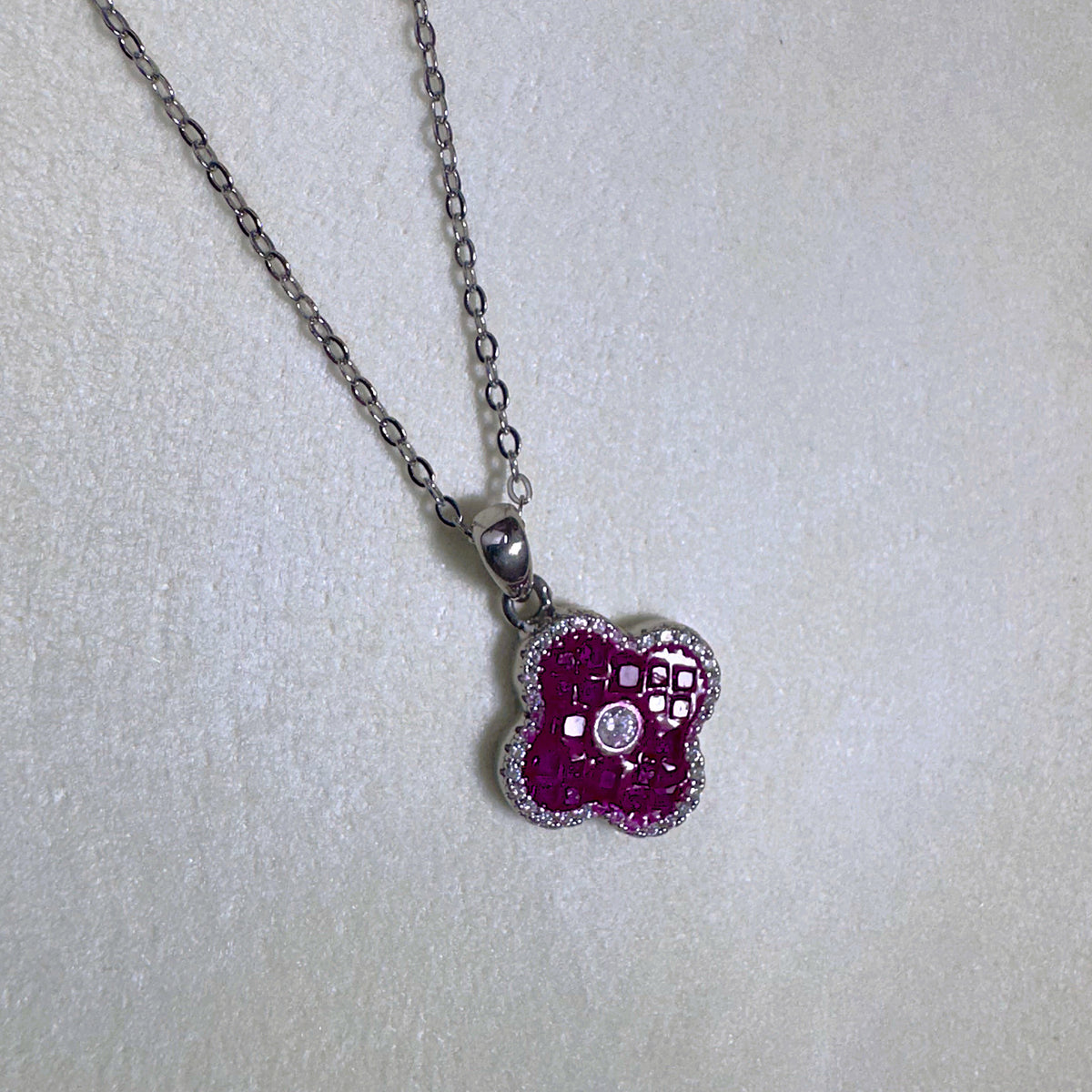 Close view of the square red glass stones and the pave border of the clover pendant.