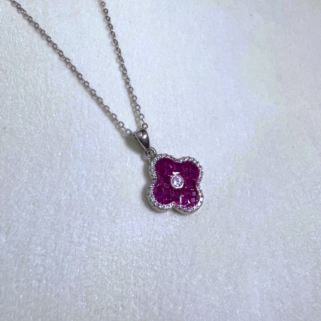 The red clover pendant necklace laid on a pale surface.