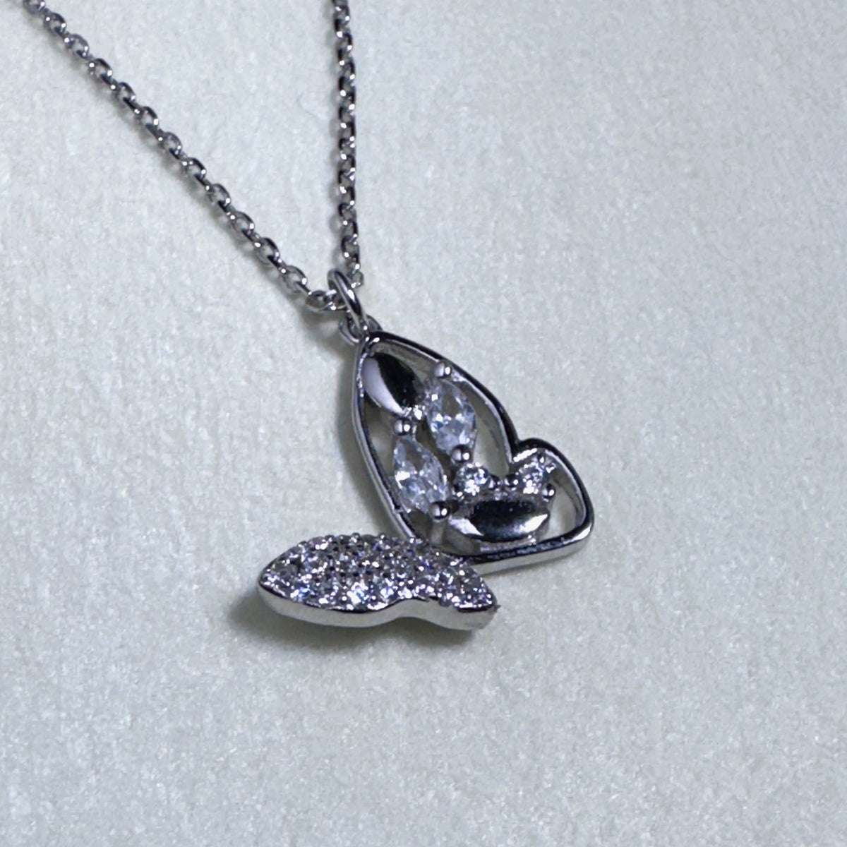 Sterling silver butterfly pendant necklace with one pave set wing and one open marquise wing, on a cable chain.