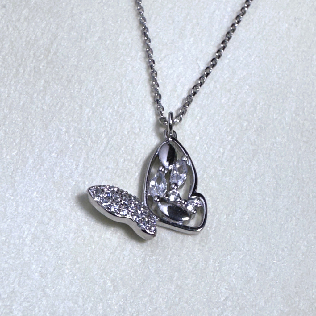 The silver butterfly pendant hanging from the cable chain on a pale surface.