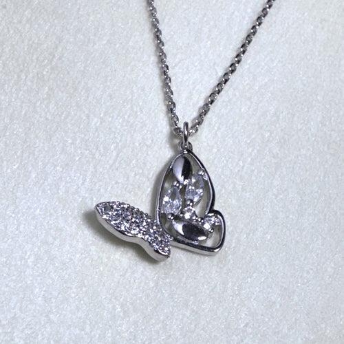 The silver butterfly pendant hanging from the cable chain on a pale surface.