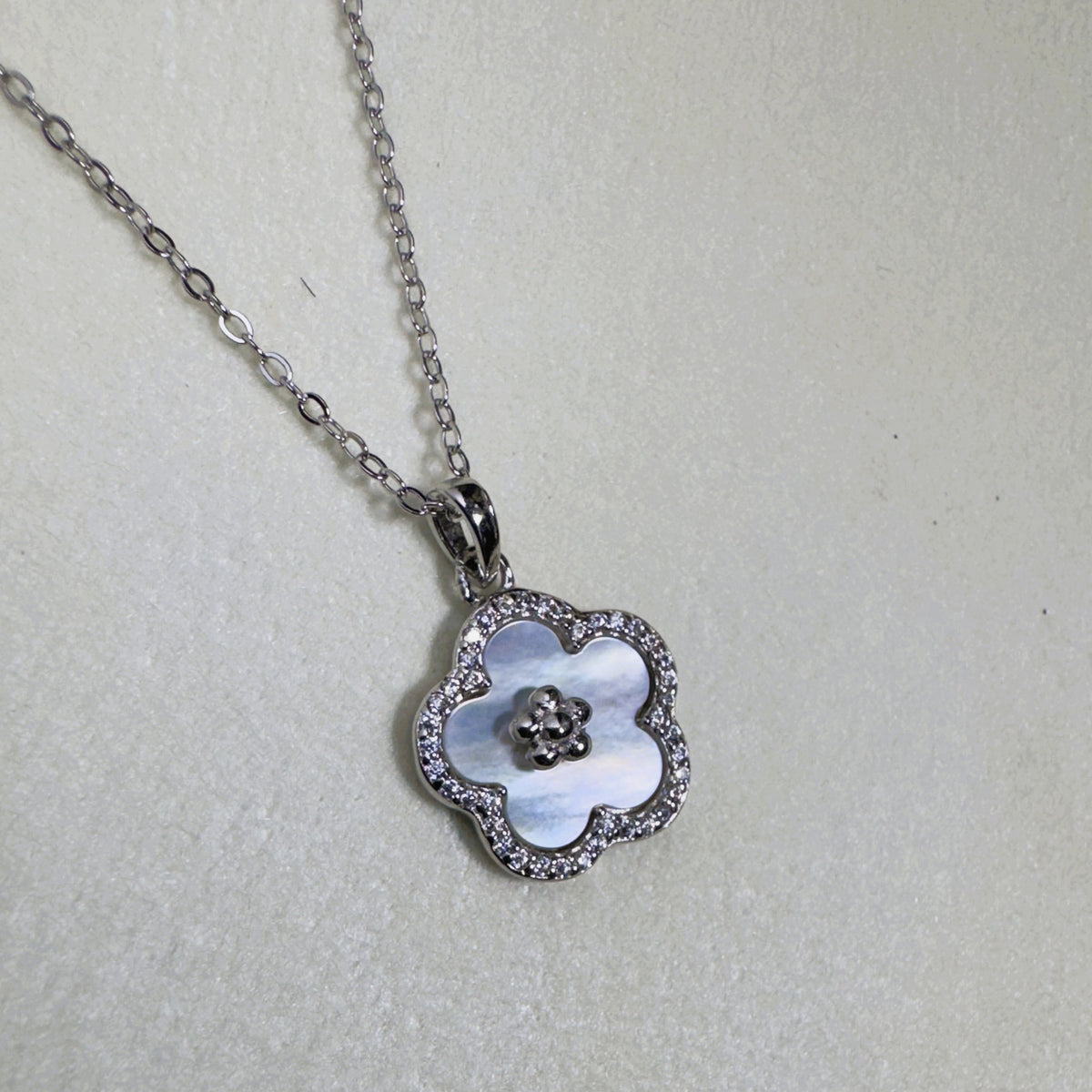 Sterling silver flower pendant necklace with a white mother of pearl face and pave border, on a cable chain.