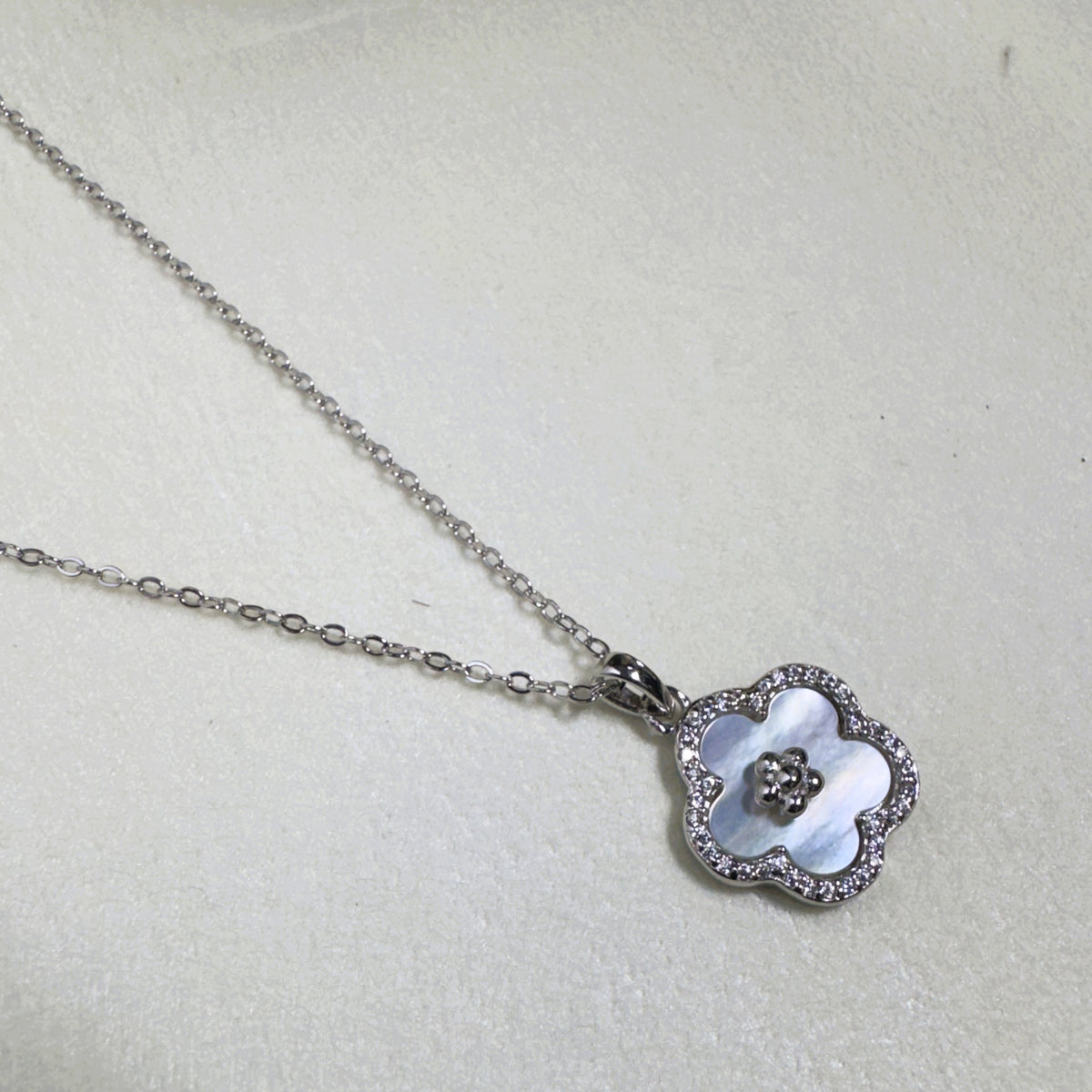 The mother of pearl flower pendant hanging from the silver cable chain.