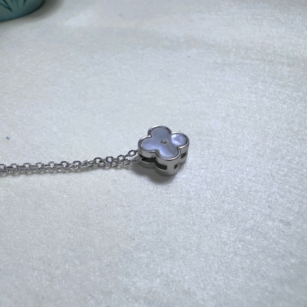 The clover slider lying on its side on the chain, showing the polished silver edge.